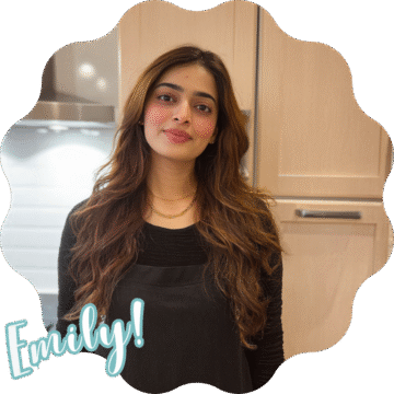 Emily smiling in a black sweater, standing in a warm kitchen, with soft lighting and a relaxed atmosphere.